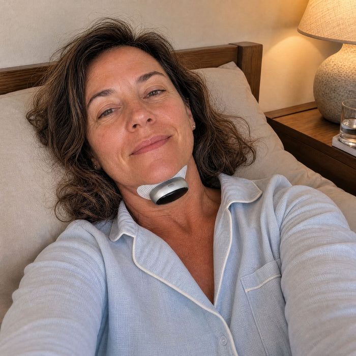 A woman lying in bed in blue pyjamas wearing the VoroHal Sleep Aid under her chin
