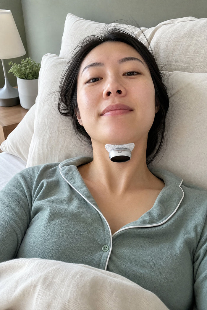 A woman settled in bed in green pyjamas wearing the VoroHal Sleep Aid under her chin