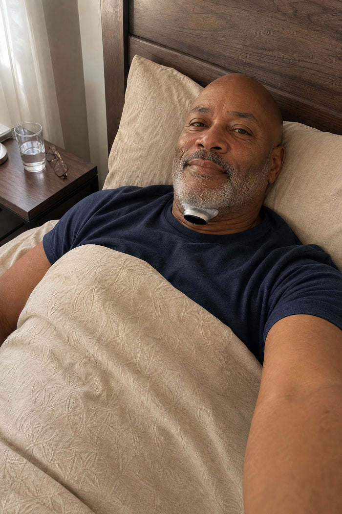 A man propped up in bed under the covers wearing the VoroHal Sleep Aid under his chin