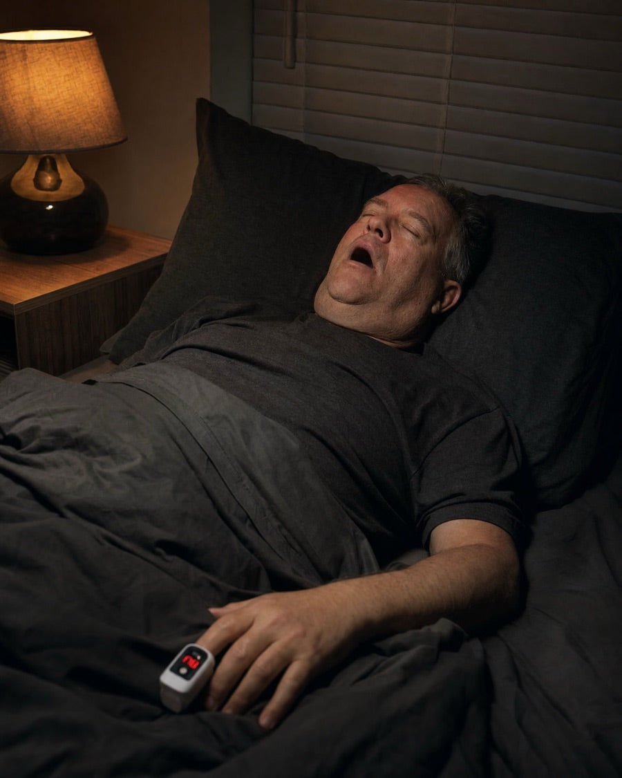 A man asleep on his back with his mouth open, a pulse oximeter on his finger